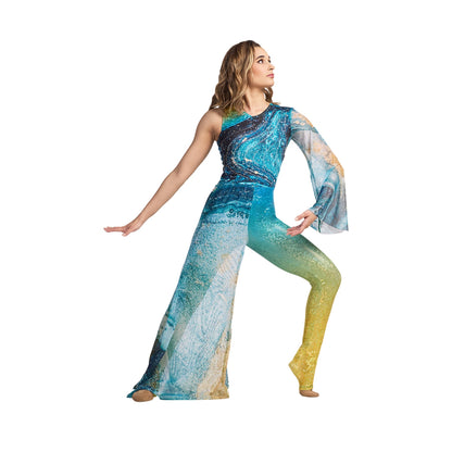 A female model wearing a sublimated hybrid jumpsuit with one mesh sleeve and wide leg, with a zipper at the back. The jumpsuit features blue and green colors with a geometric pattern and rhinestone embellishments.