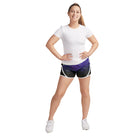 Model wearing S‑Line paneled performance shorts in black with white piping trim and purple geometric panel, mid-rise fit with elastic waistband—styled for dance, drill, or color guard
